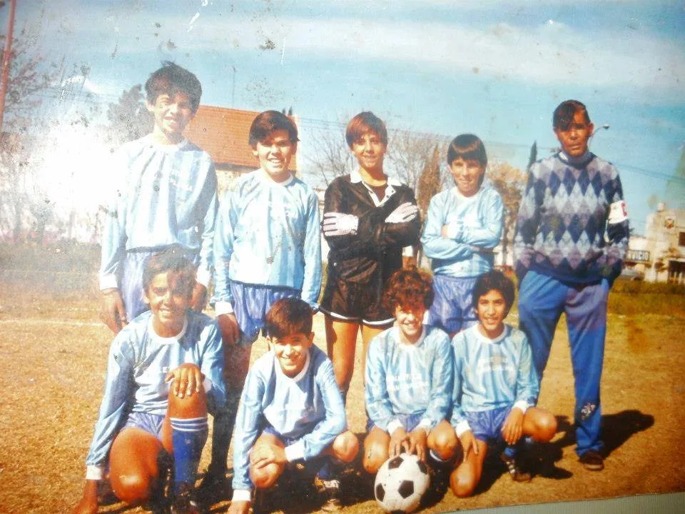 Foto antigua de un plantel de chicos del Club Universitario de Berisso posando en la cancha con la camiseta celeste y blanca, junto a su entrenador